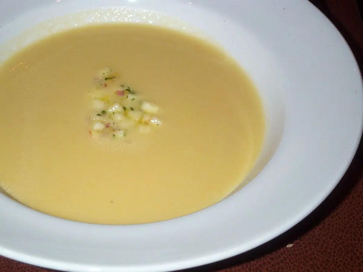 Plato hondo blanco de crema amarilla de chirivía con un montoncito de manzana picada encima