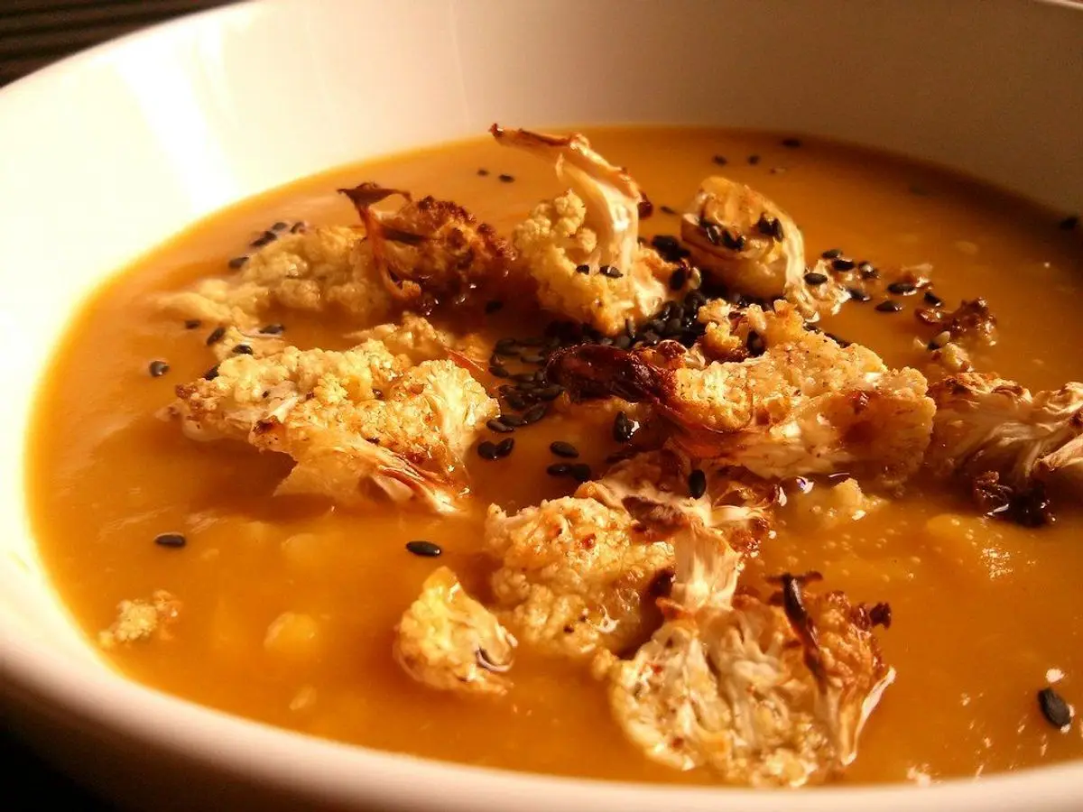 Plato hondo de crema anaranjada especiada con coliflor tostada por encima