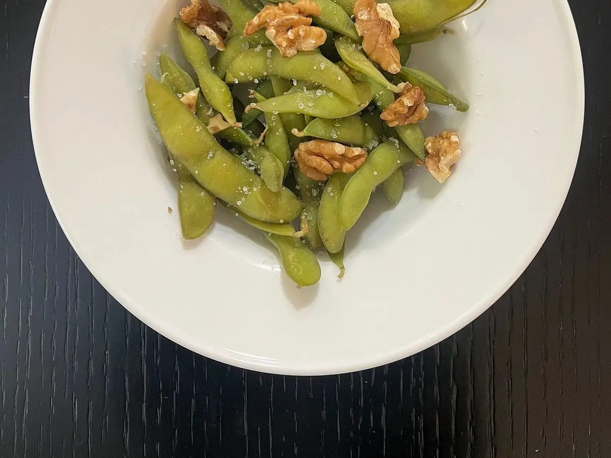 Plato blanco con vainas de edamame y nueces sobre una mesa oscura
