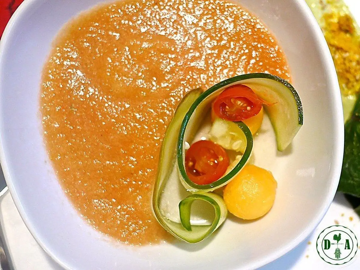 Plato blanco de crema fría anaranjada con cinta de pepino y tomate cherry como guarnición