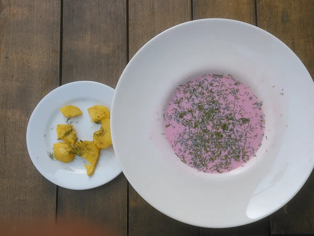 Plato hondo blanco de crema fría rosa de remolacha con hierbas, junto a un plato pequeño