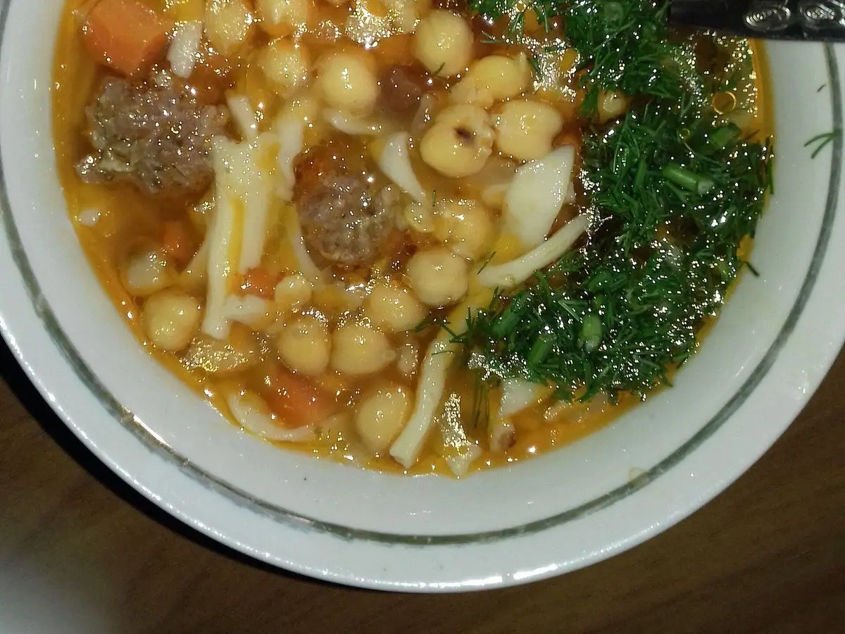 Plato hondo de sopa de garbanzos con trozos de carne, zanahoria y eneldo fresco