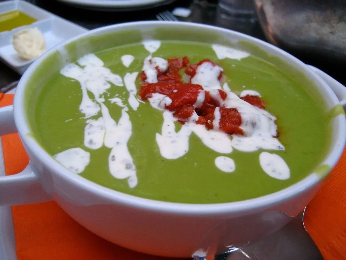 Cuenco de crema verde de guisantes con nata y daditos rojos por encima