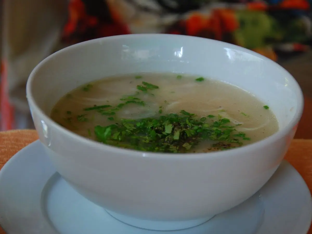 Cuenco blanco de crema clara de hinojo con perejil picado sobre un plato azul