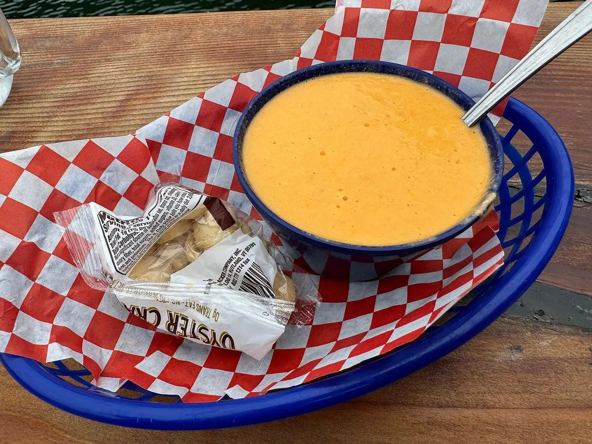 Cuenco azul de crema anaranjada de marisco sobre una cesta con papel de cuadros rojos y blancos