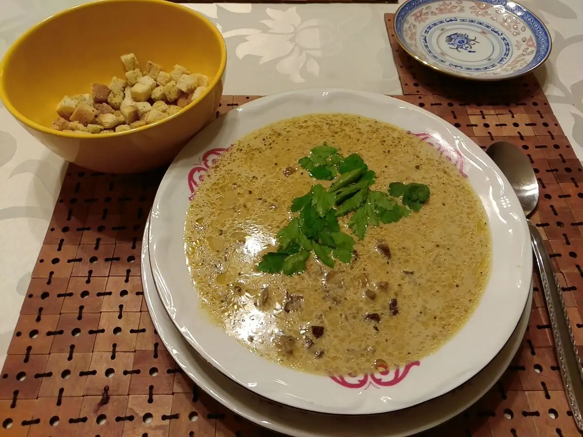 Plato hondo de crema de setas con hojas de perejil y un cuenco de picatostes al lado