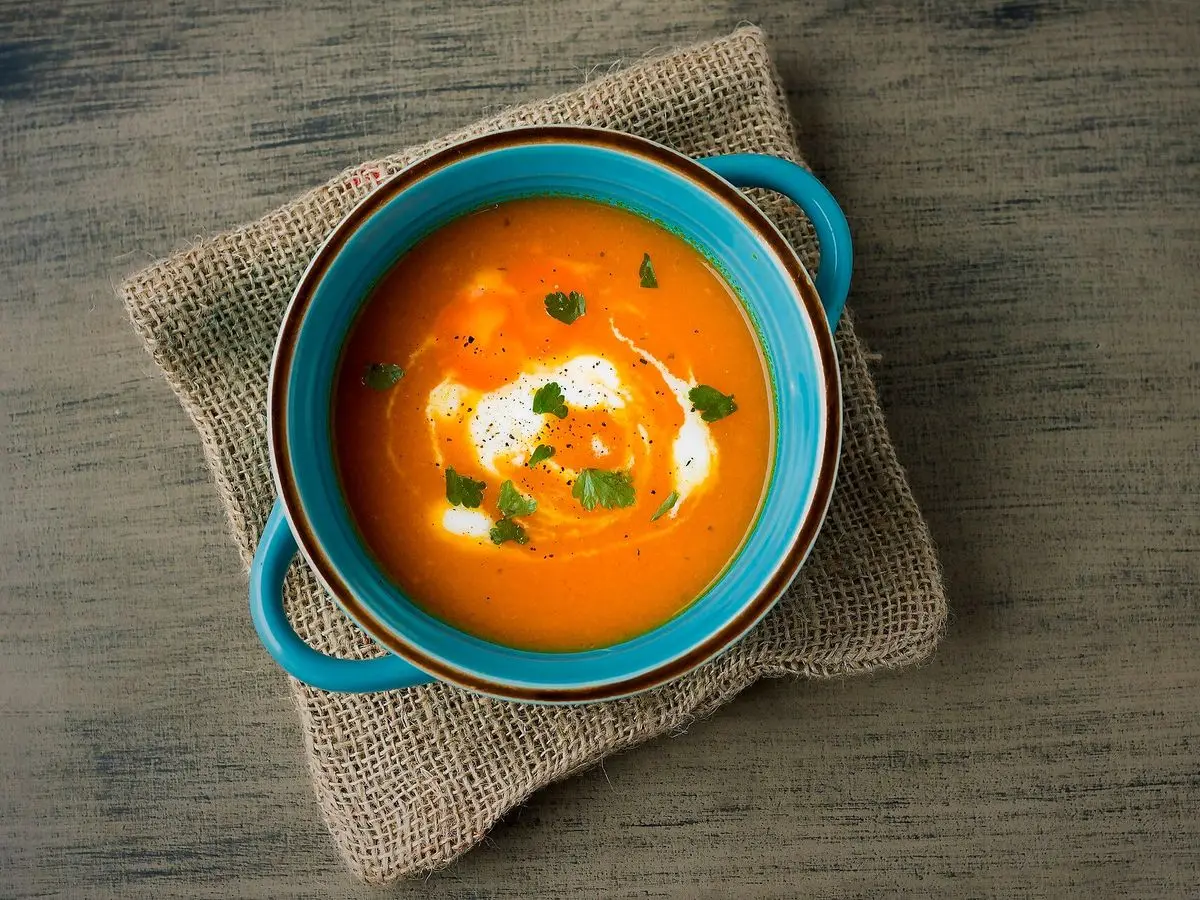 Cuenco azul de crema anaranjada de zanahoria con un toque de nata y hierbas sobre una tela