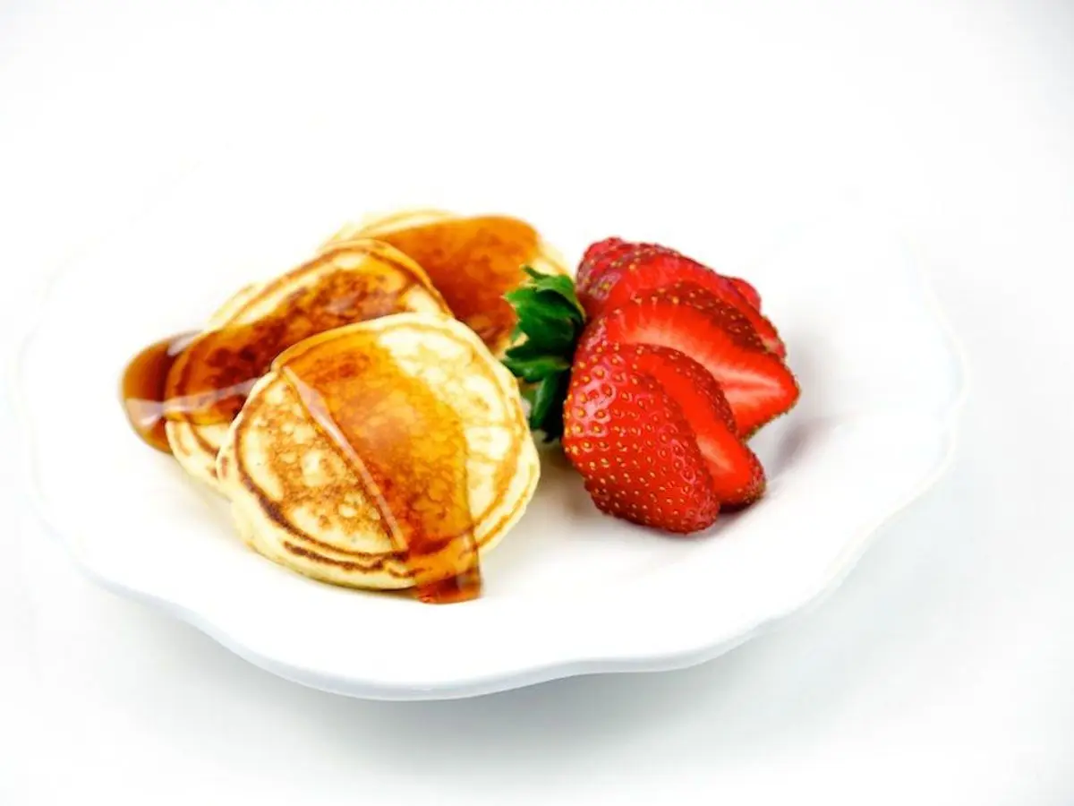 Tortitas pequeñas con almíbar y fresas frescas en un plato blanco sobre fondo claro
