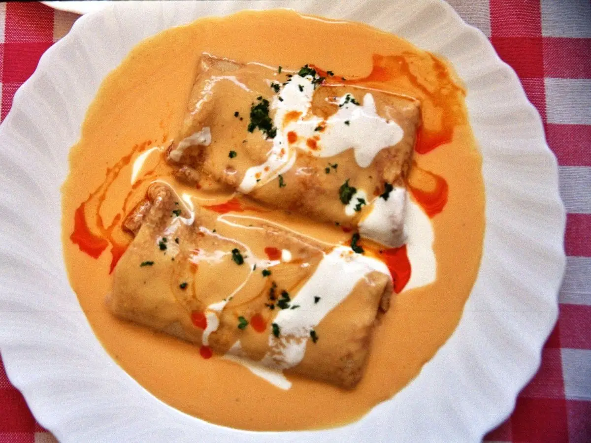 Crepes rellenos en salsa anaranjada de pimentón con nata agria sobre un plato blanco