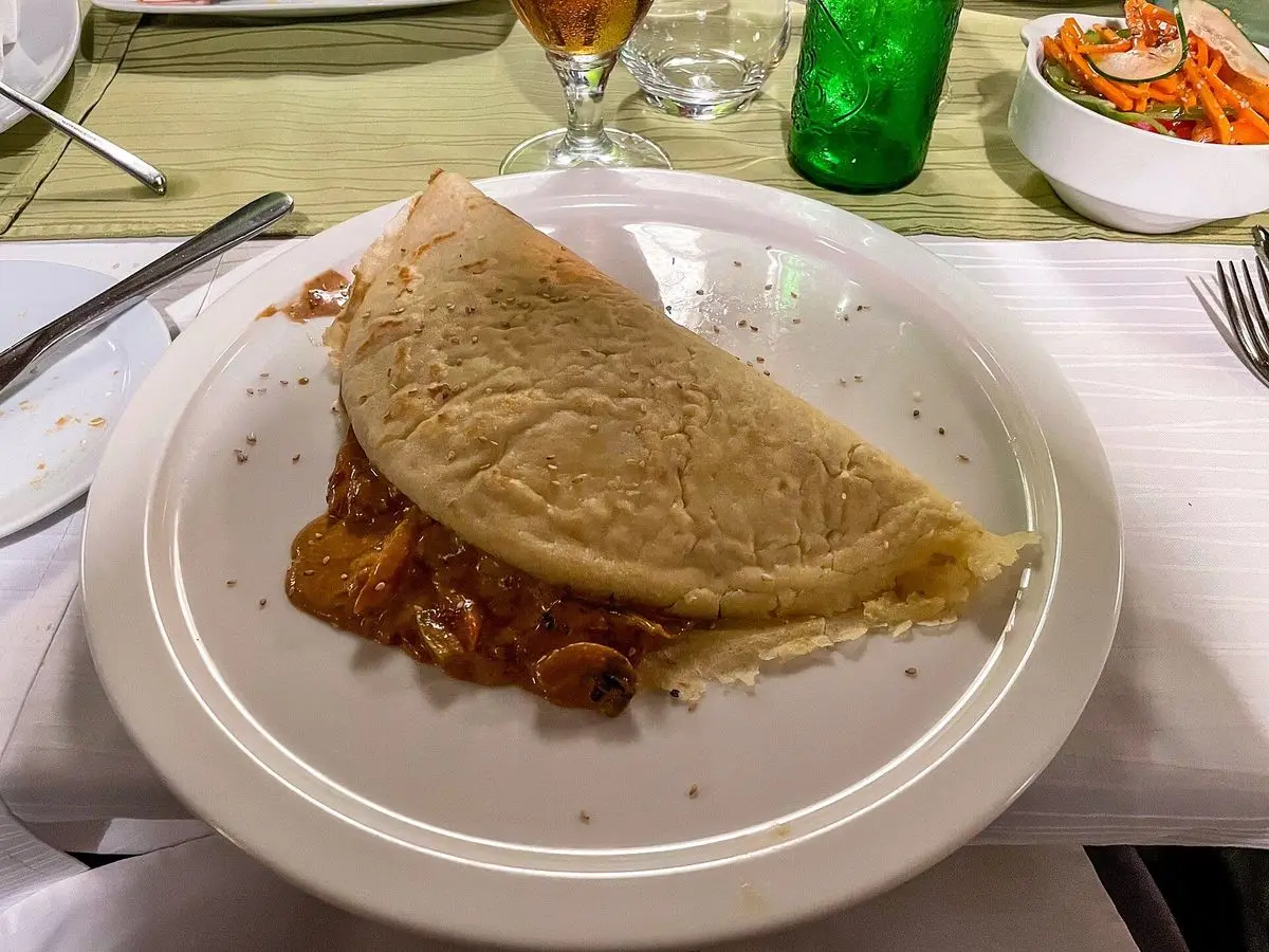 Crepe salado doblado relleno de guiso de tomate en un plato blanco sobre un mantel