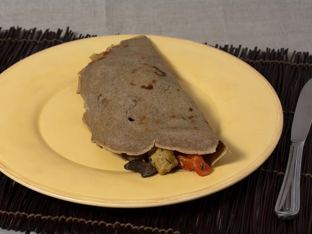 Crepe oscuro de trigo sarraceno doblado con relleno de verduras sobre un plato amarillo