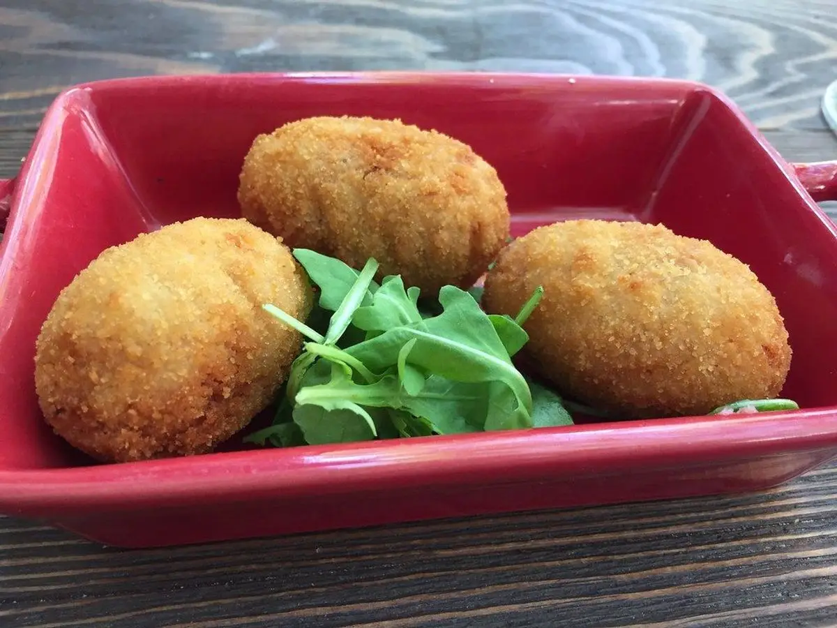 Tres croquetas doradas en un cuenco rojo con hojas de rúcula