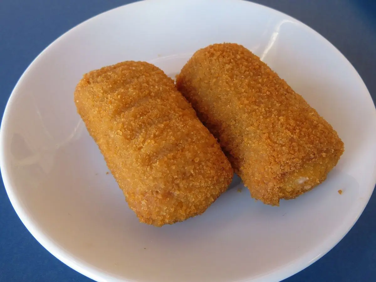 Dos croquetas doradas y empanadas sobre un plato blanco