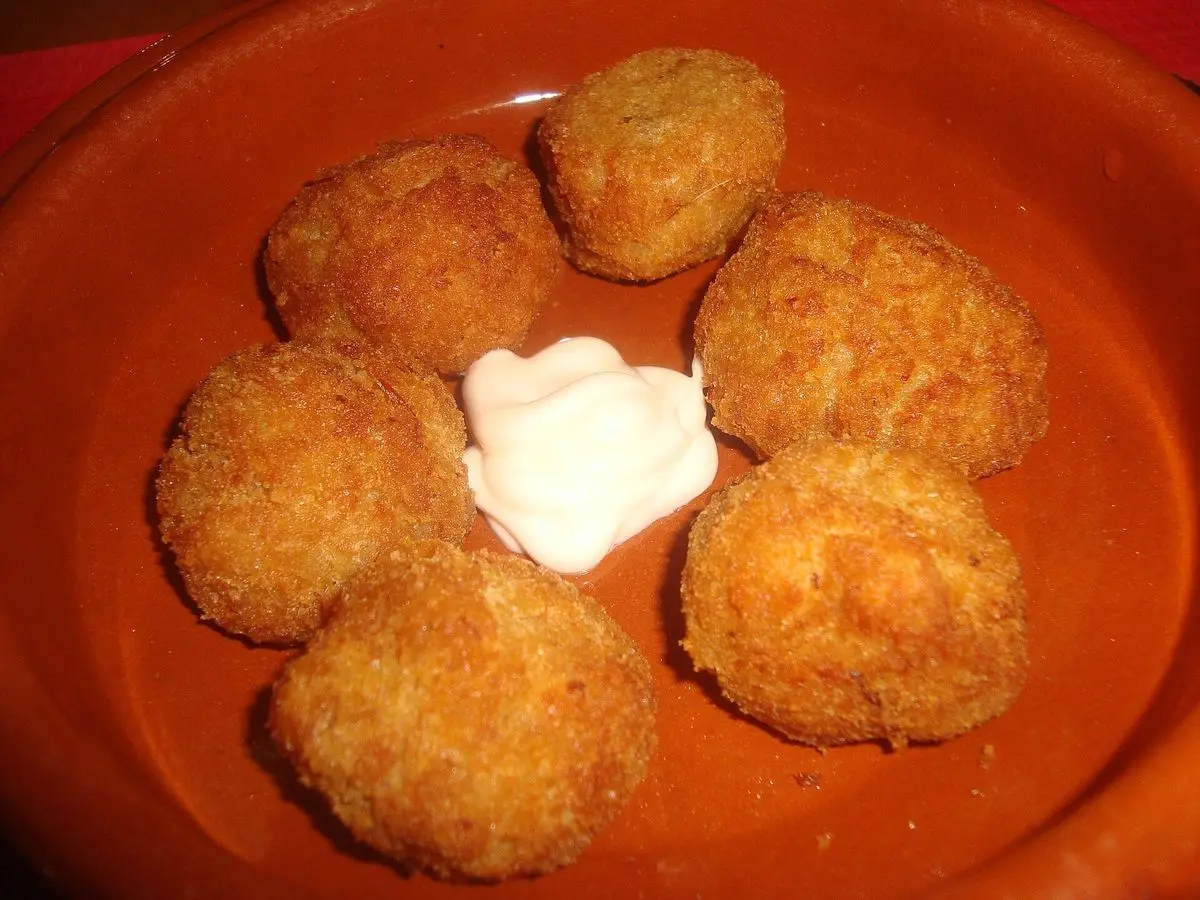 Croquetas doradas sobre un plato de barro con una cucharada de salsa blanca