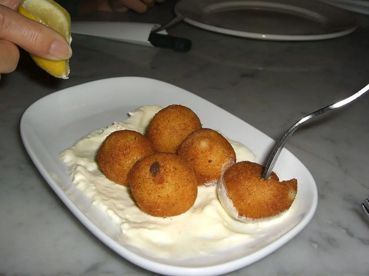 Croquetas doradas sobre una salsa blanca cremosa en un plato ovalado blanco
