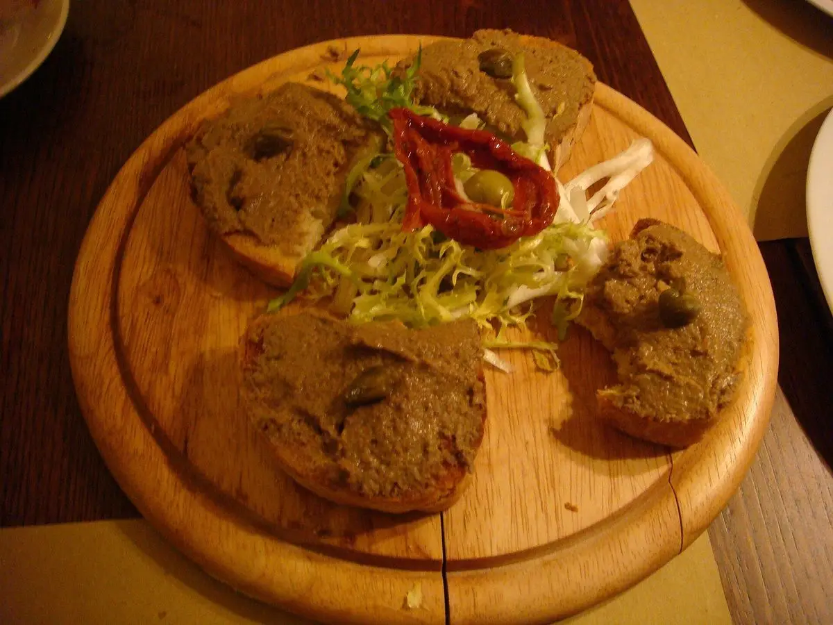 Tabla redonda de madera con crostini toscani untados de paté de hígado y un poco de ensalada