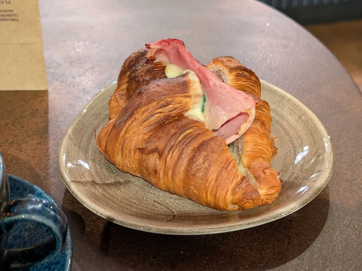 Cruasán relleno de jamón y queso en un plato sobre una mesa de cafetería