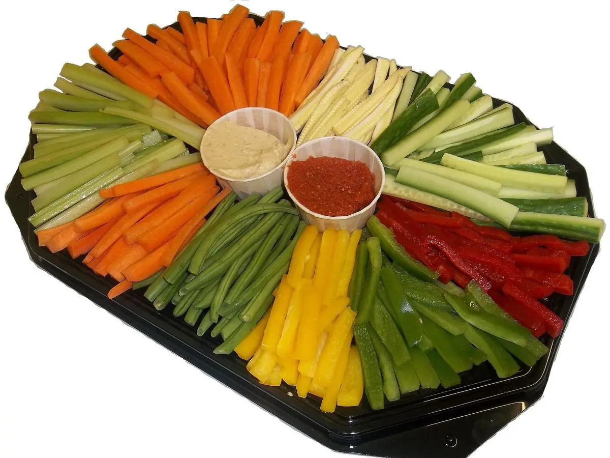Bandeja de crudités con bastones de zanahoria, pepino y pimiento amarillo y rojo con dos salsas