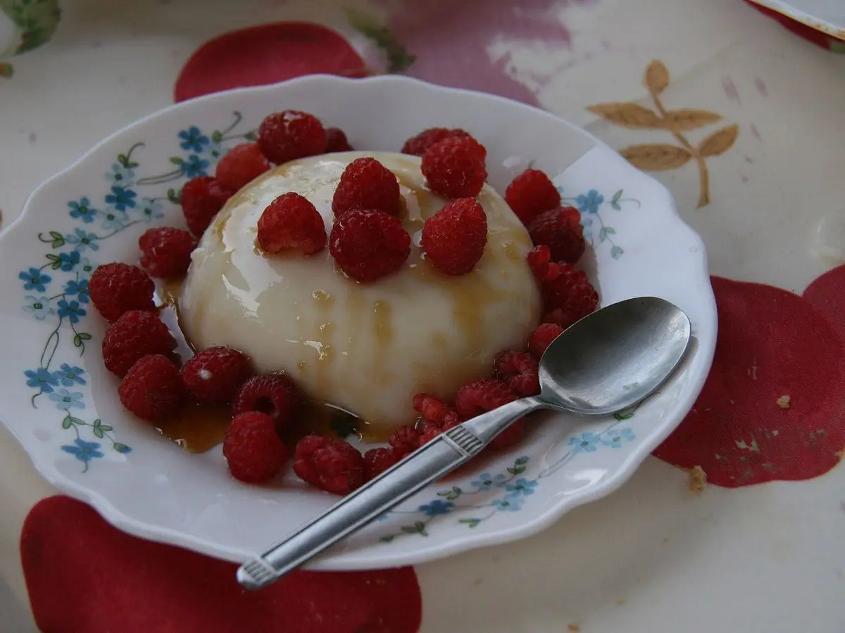 Cuajada blanca con frambuesas frescas y miel en un plato de flores con cuchara