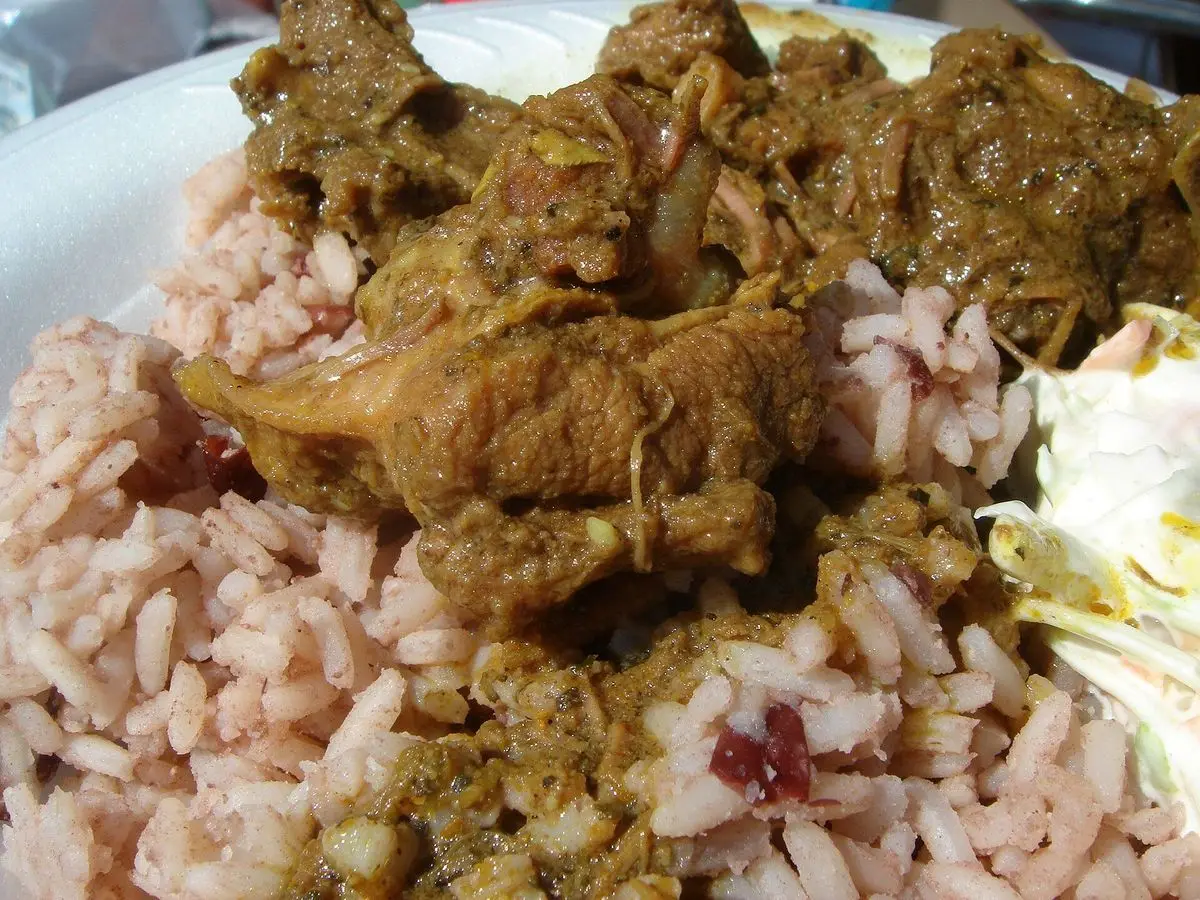 Plato de cabrito al curry con arroz y alubias, con una hoja de lechuga