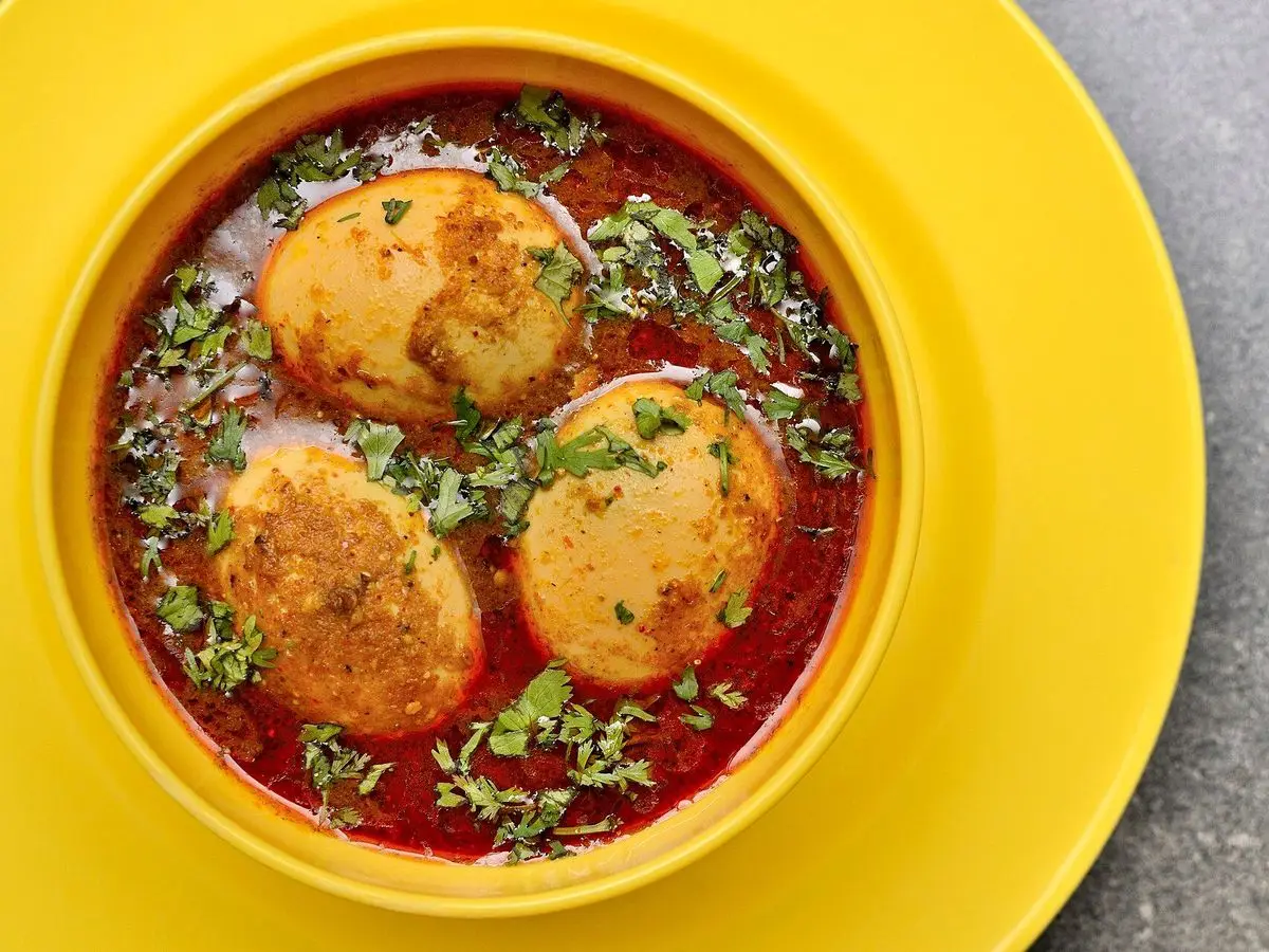 Cuenco amarillo con curry de huevos duros en salsa roja de tomate y cilantro picado