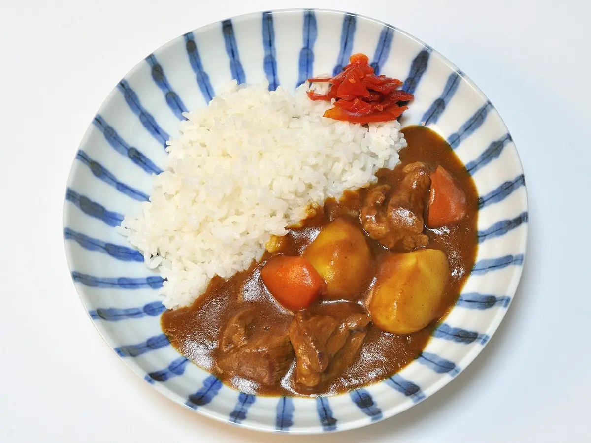 Plato de curry japonés con patata, zanahoria y carne guisada junto a arroz blanco en un plato de rayas azules