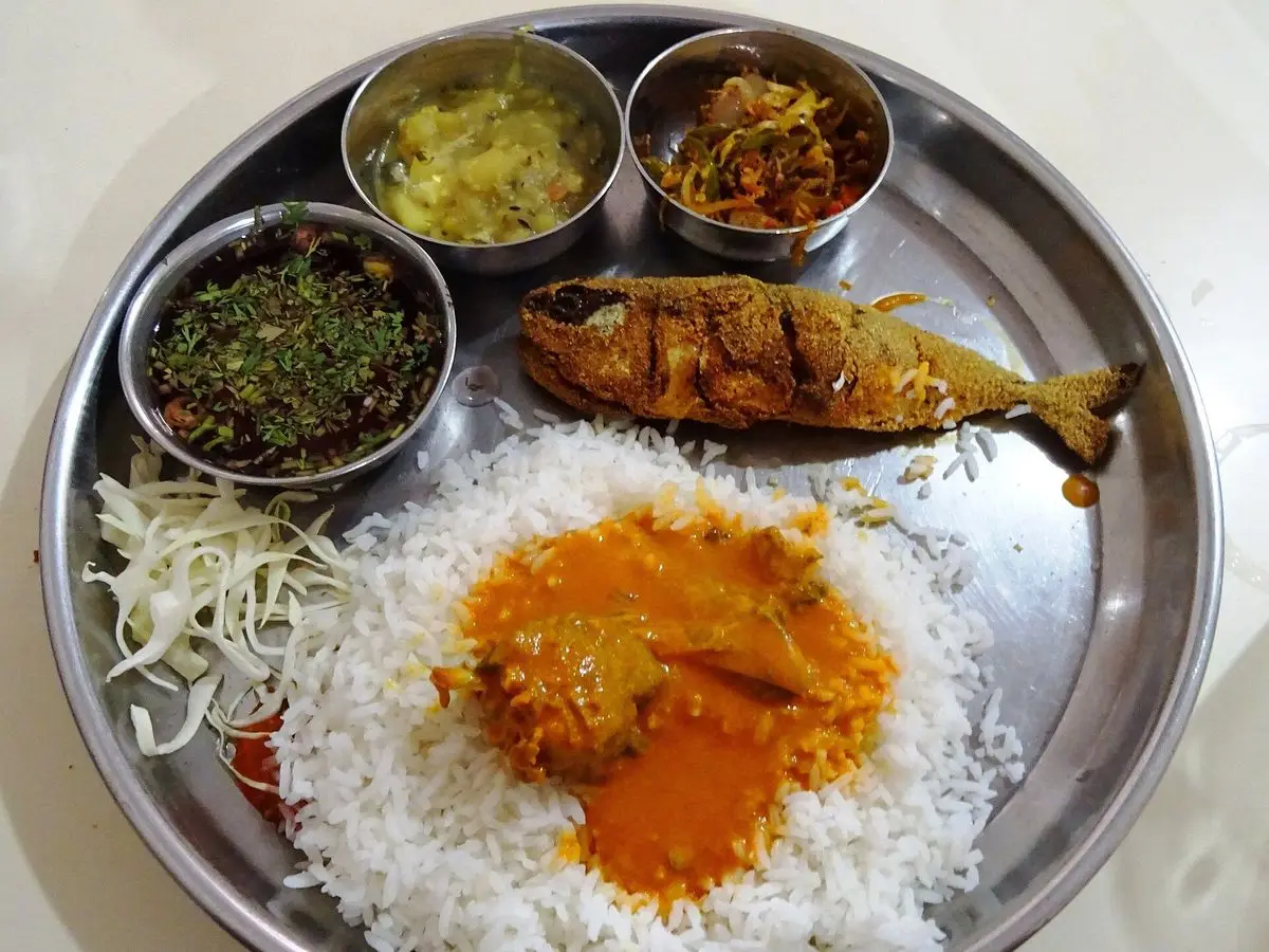 Bandeja metálica con arroz blanco, curry de pescado anaranjado, pescado frito y guarniciones