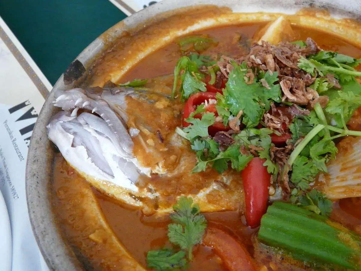 Fuente de curry rojo de cabeza de pescado con okra, tomate y cilantro