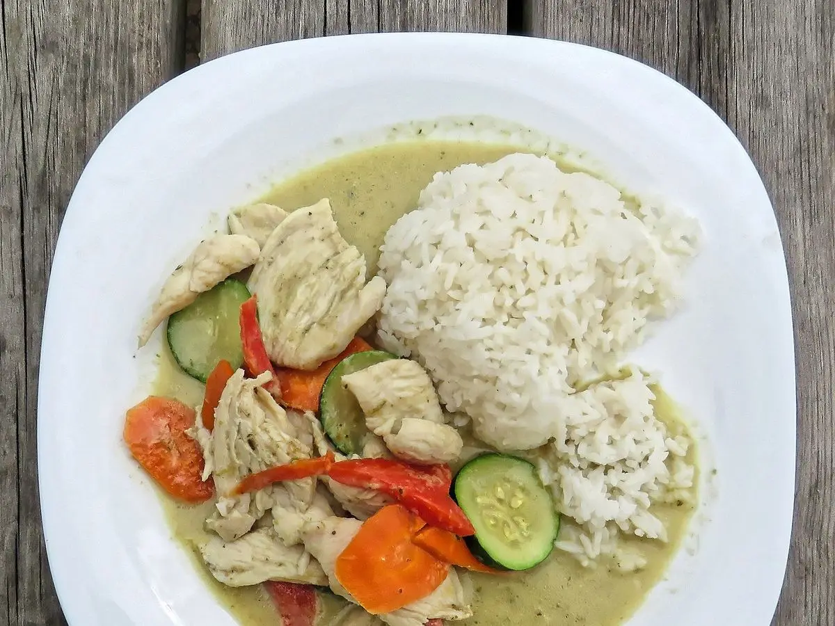 Curry verde de pollo con verduras junto a arroz blanco en un plato blanco