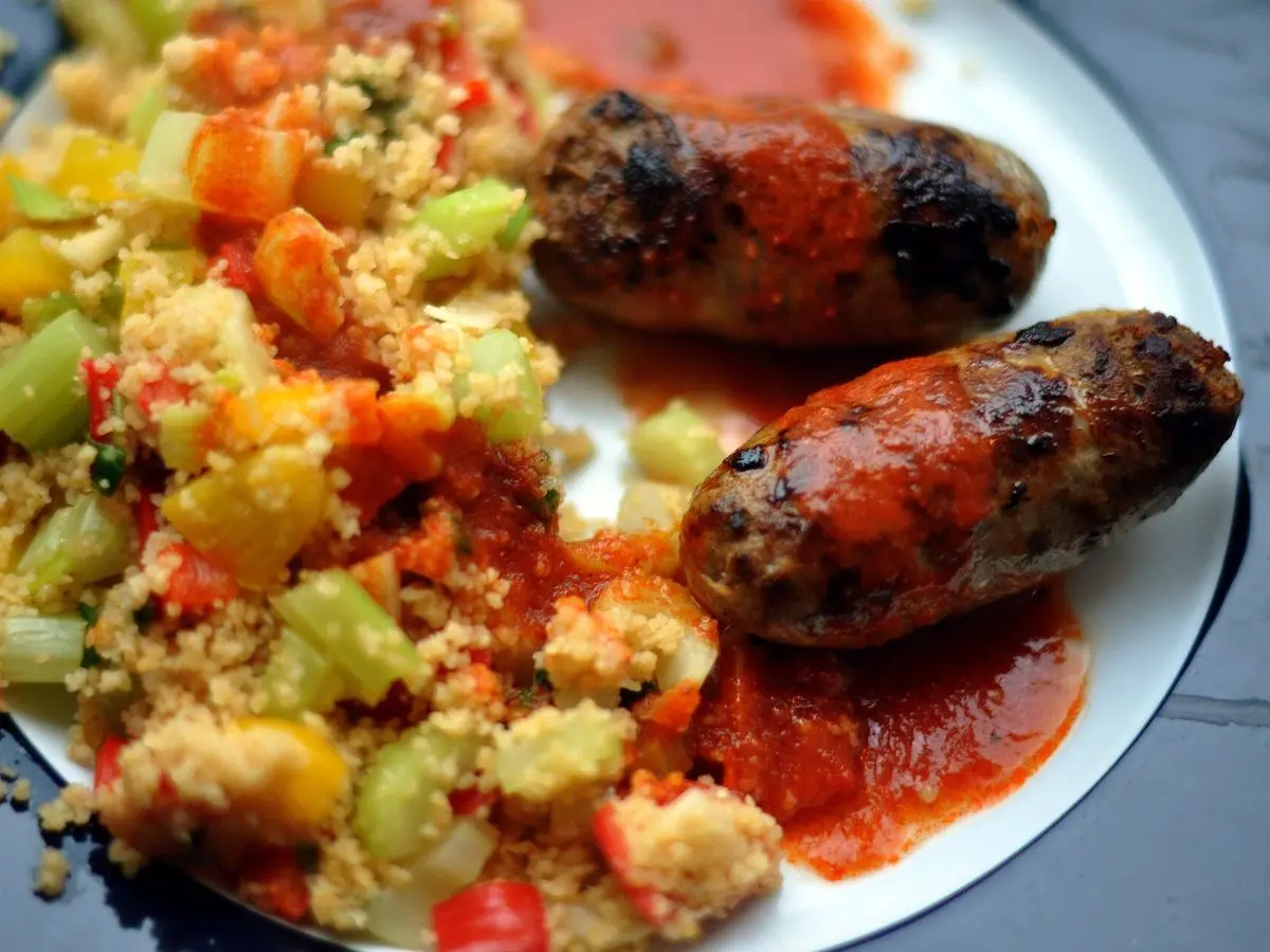 Cuscús con verduras en dados y dos salchichas merguez a la parrilla con salsa roja