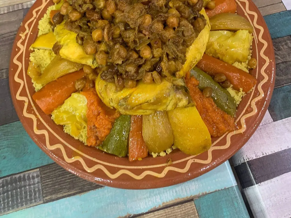 Fuente de barro con cuscús cubierto de garbanzos y verduras amarillas y anaranjadas