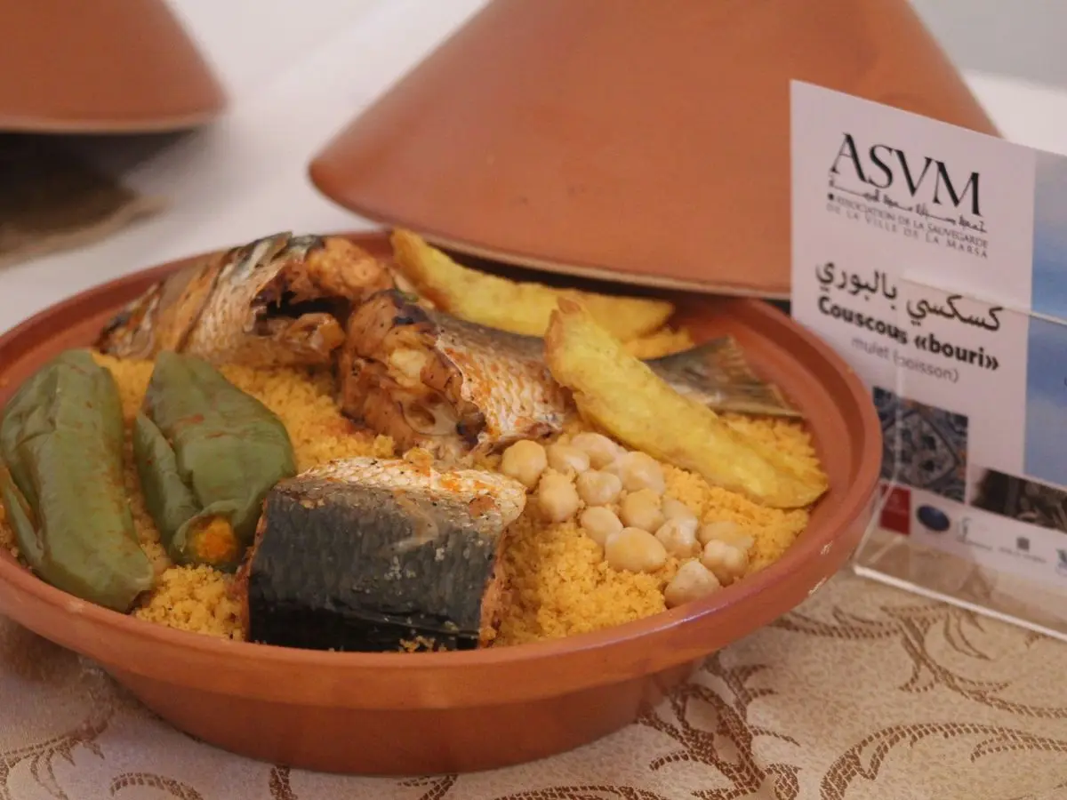 Cuscús tunecino con pescado y verduras servido en una fuente de barro con tapa cónica