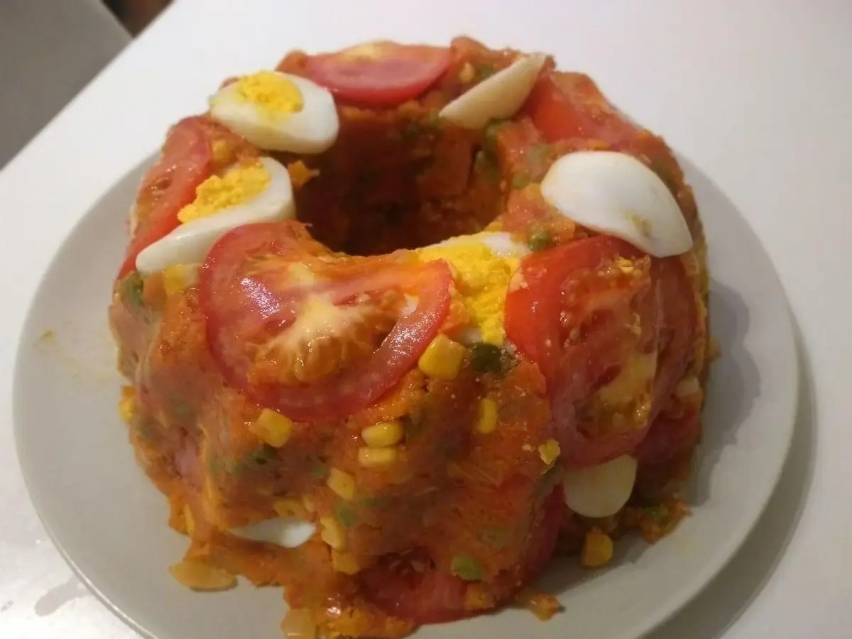 Corona de cuscús de maíz amarillo con rodajas de tomate y huevo cocido sobre un plato blanco