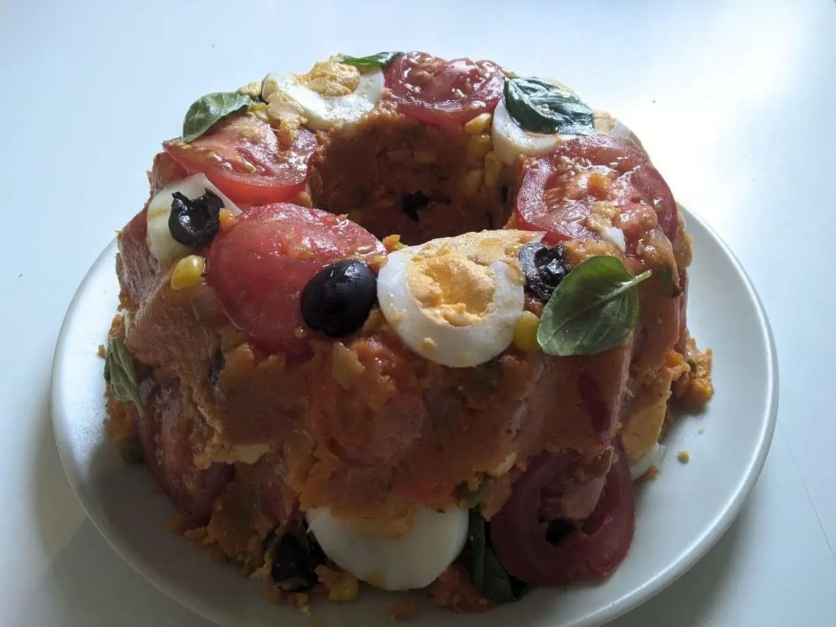 Cuscús paulista en forma de corona con tomate, aceitunas negras y huevo duro en un plato blanco