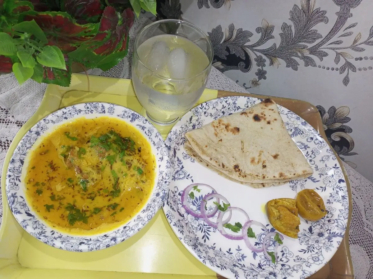 Plato de dal amarillo de lentejas con cilantro, junto a pan chapati y aros de cebolla roja