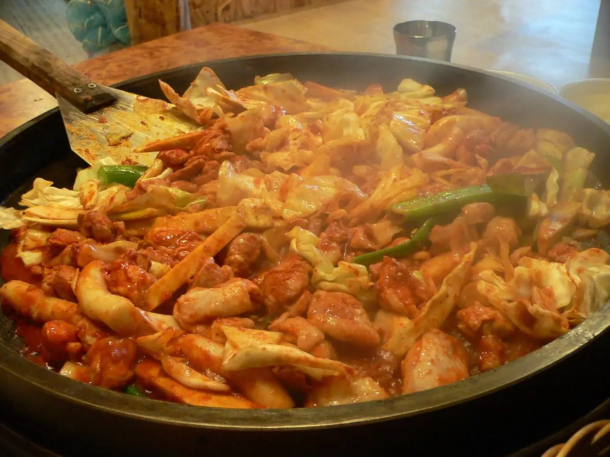 Sartén de pollo picante con col y salsa roja chisporroteando sobre una plancha negra