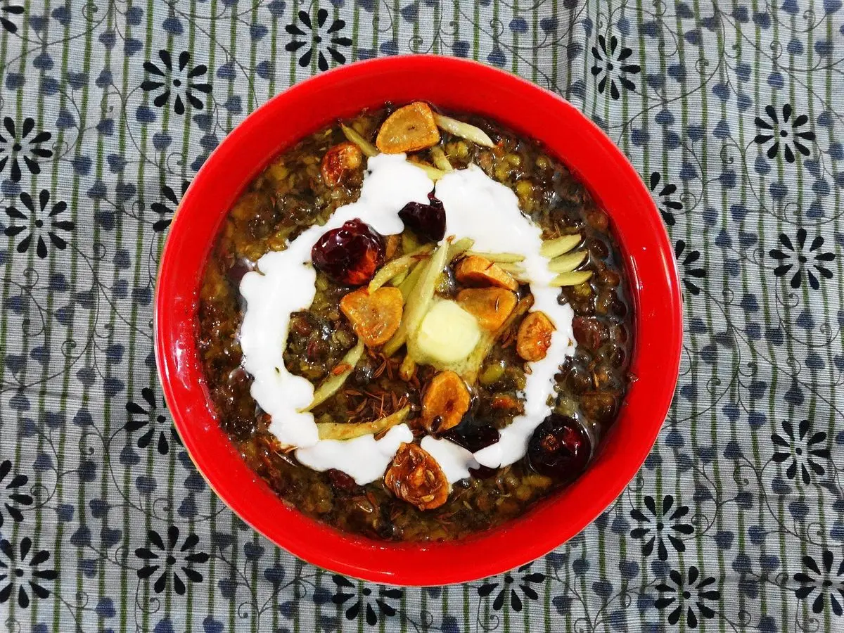 Cuenco rojo de dal makhani de lentejas oscuras con nata y frutos secos sobre un mantel estampado