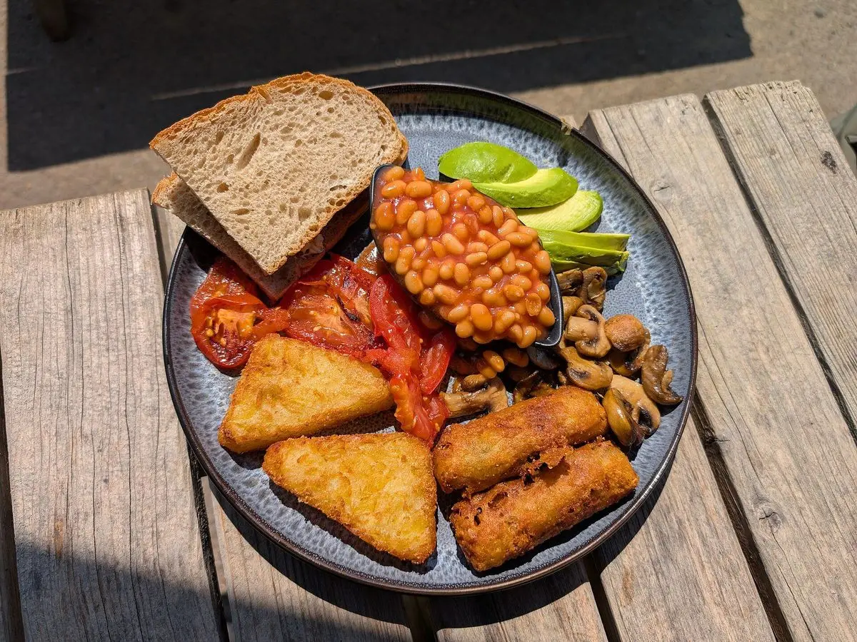 Plato de desayuno vegano con alubias en salsa de tomate, tostada de pan, aguacate y croquetas vegetales