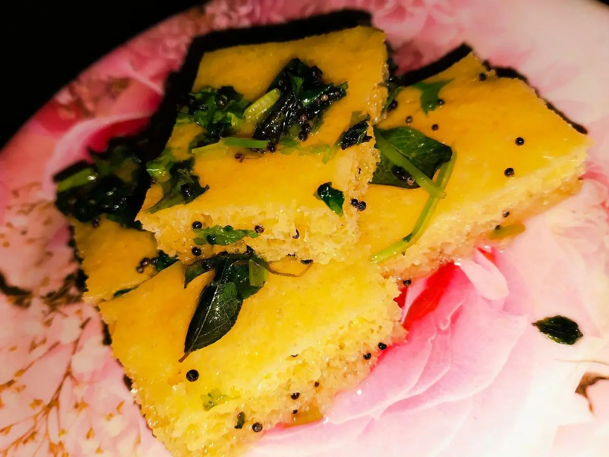 Cuadrados amarillos de dhokla, bizcocho esponjoso de garbanzo, con hojas de curry y mostaza sobre un plato de flores