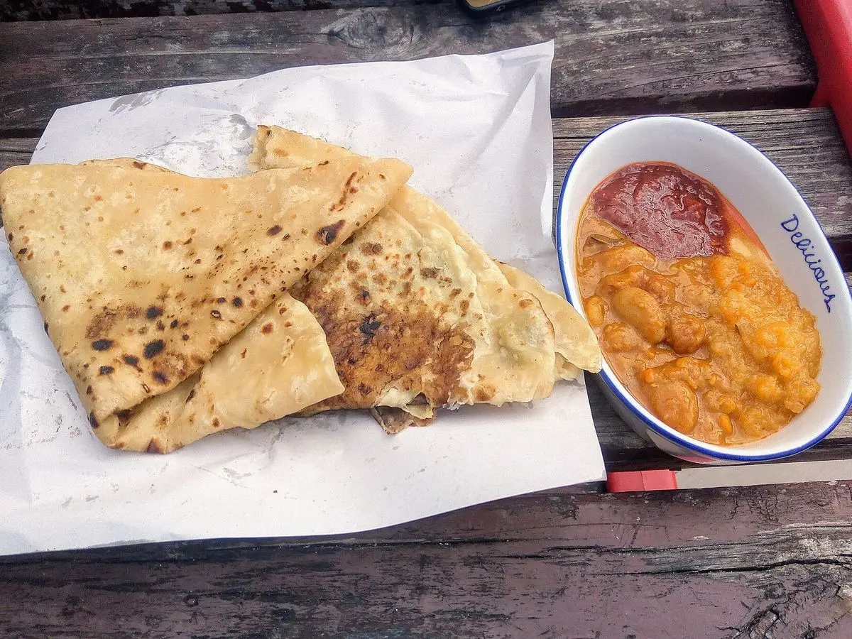 Dholl puri doblados sobre papel junto a un cuenco de salsa anaranjada de tomate