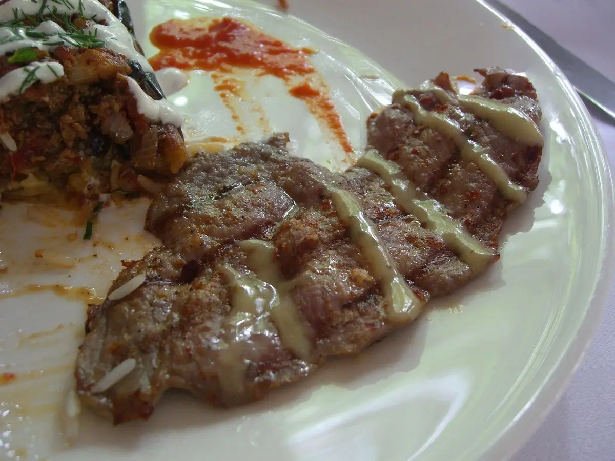 Tiras de carne asada a la parrilla con un hilo de salsa de mostaza en un plato blanco