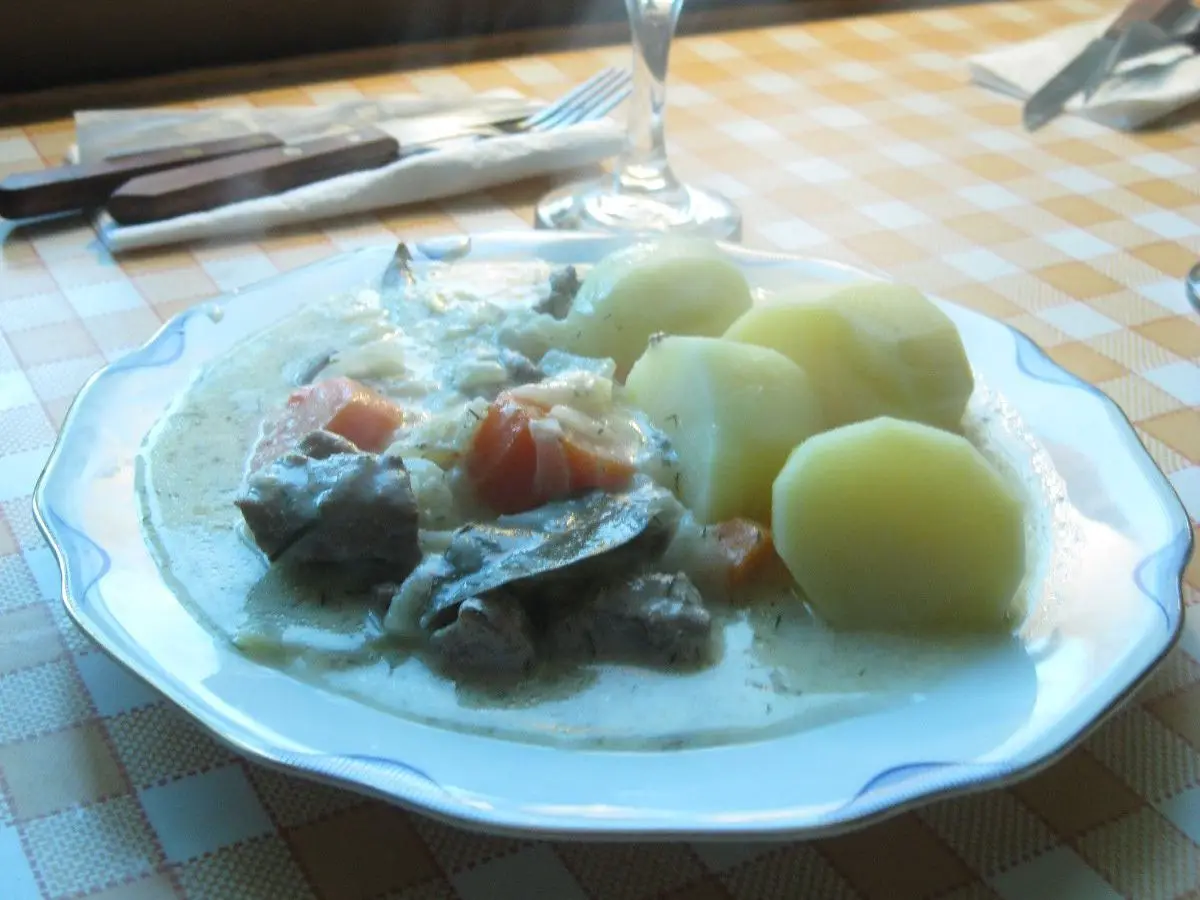 Plato con carne en salsa cremosa de eneldo, zanahoria y patatas cocidas sobre un mantel de cuadros