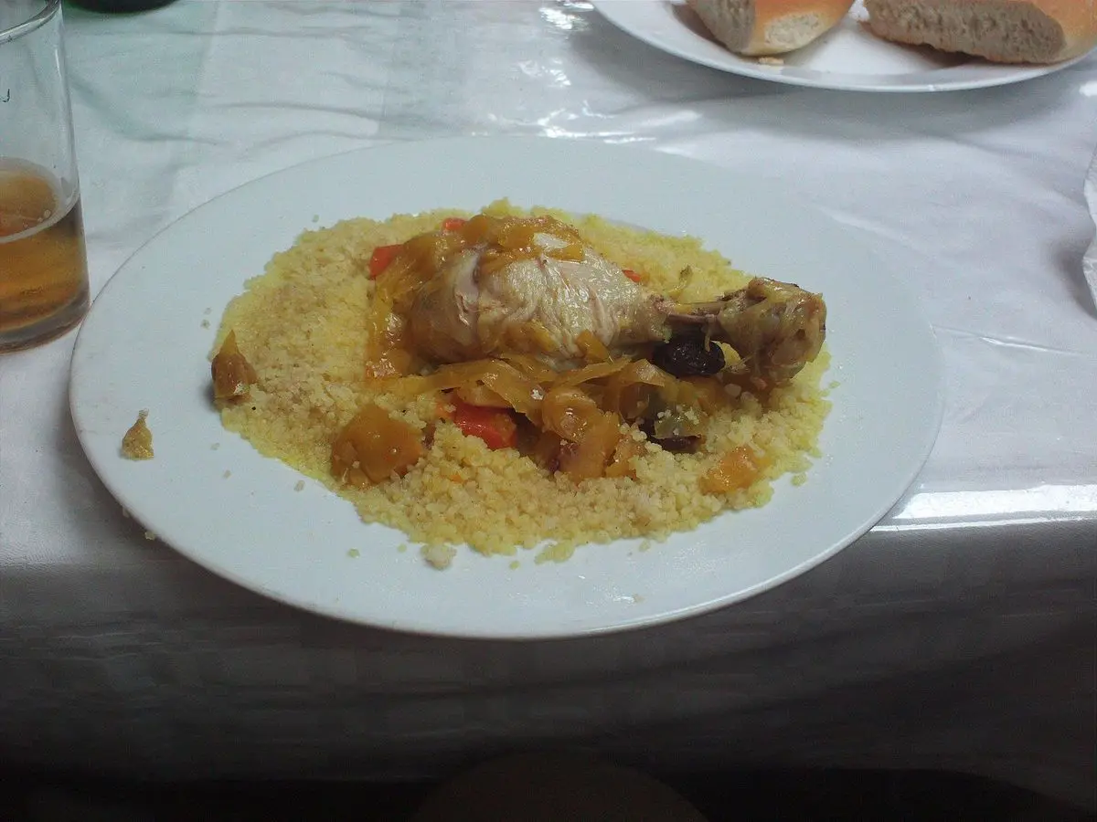 Pollo guisado sobre cuscús amarillo azafranado en un plato blanco sobre mantel
