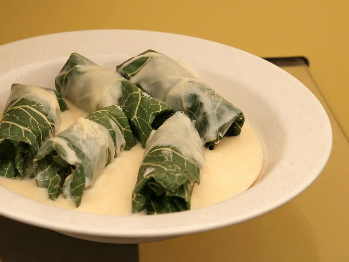 Plato hondo con rollitos rellenos envueltos en hojas de acelga sobre una salsa cremosa blanca