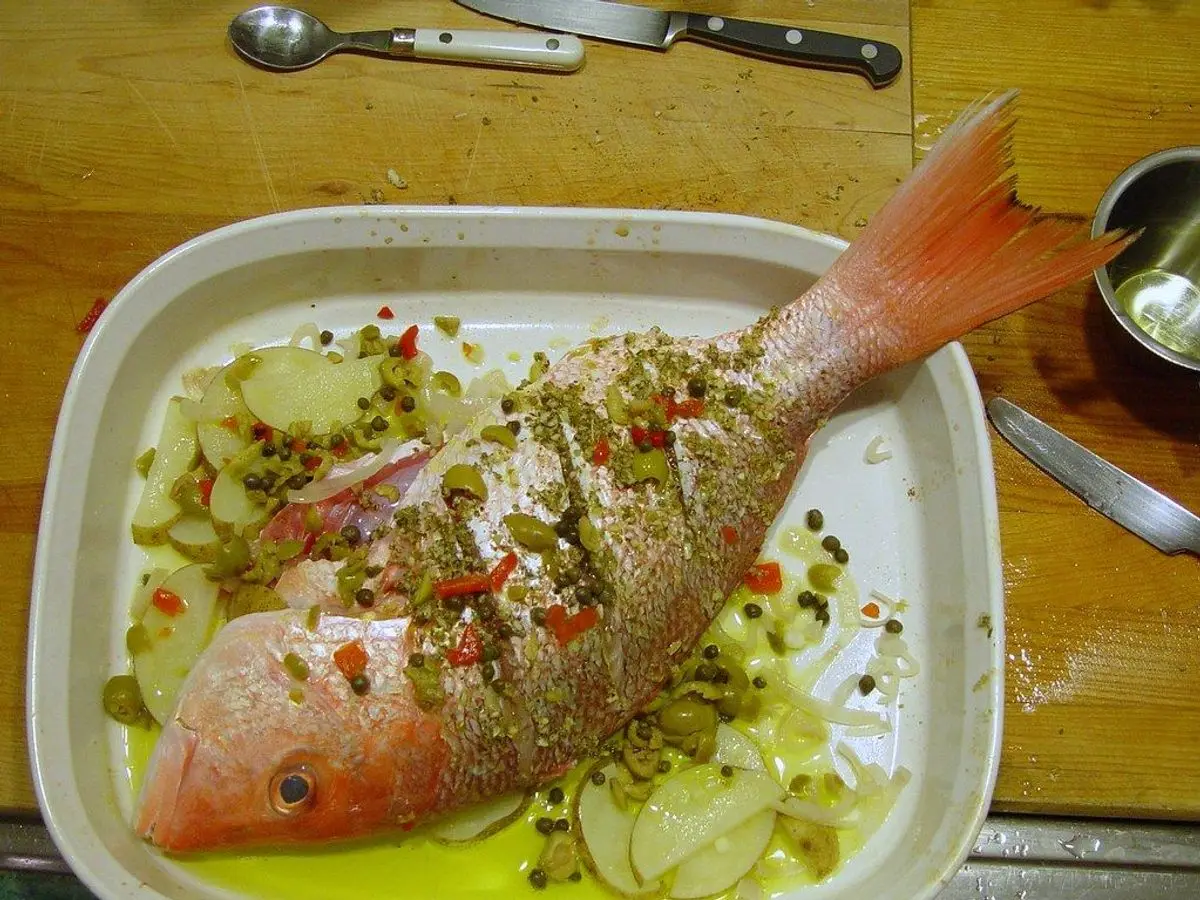 Pescado entero asado con hierbas y verduras en una fuente blanca rectangular sobre una mesa de madera