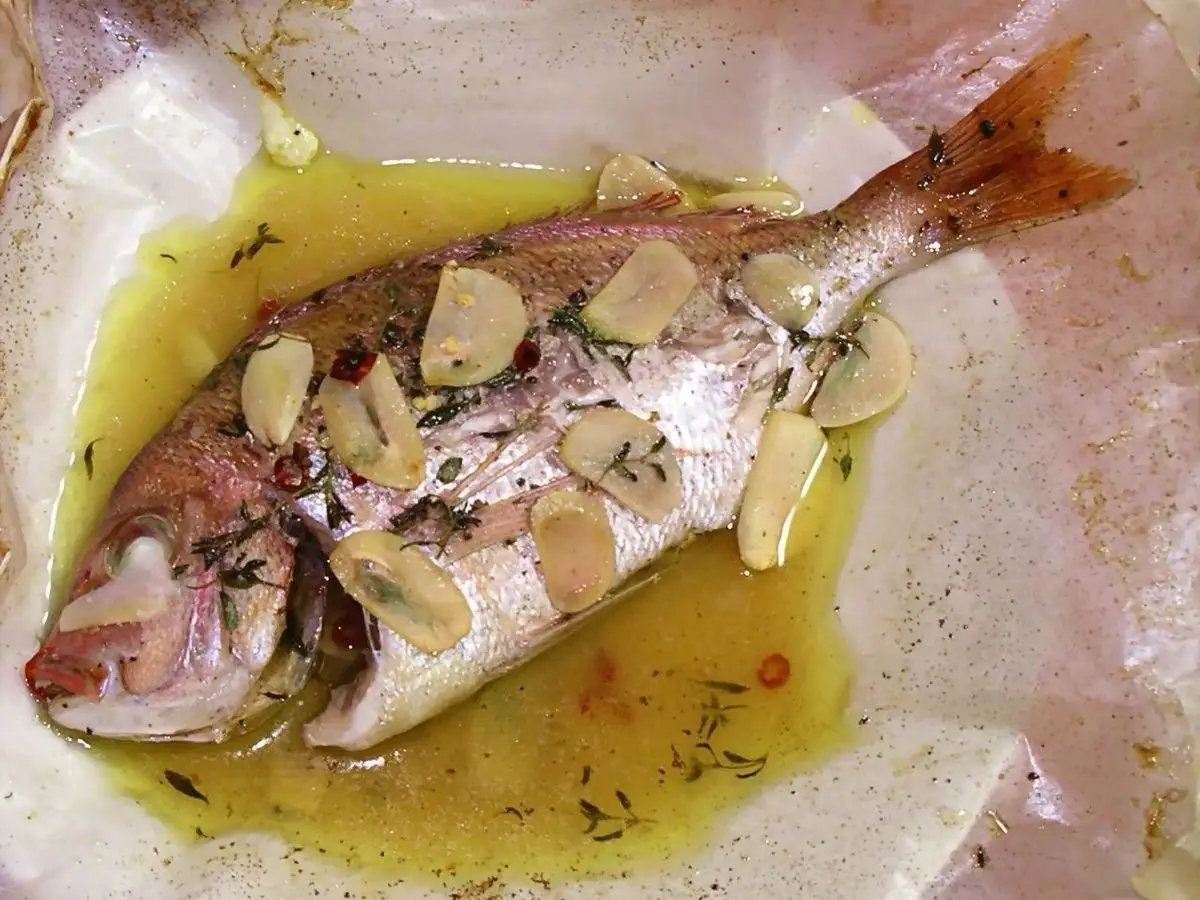 Dorada entera al cartoccio sobre papel de horno con aceite, láminas de ajo y hierbas