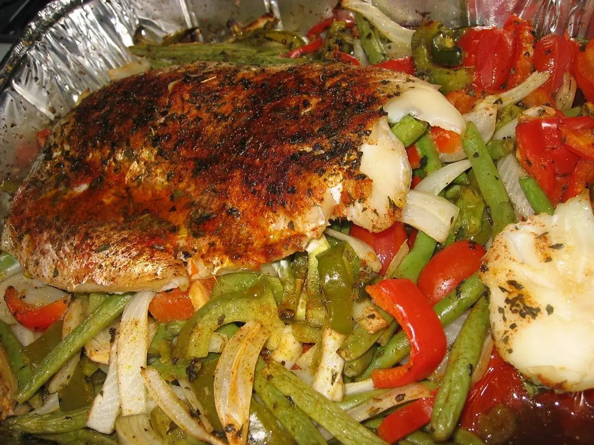 Filete de pescado al horno sobre una cama de pimientos, cebolla y judías verdes en una bandeja