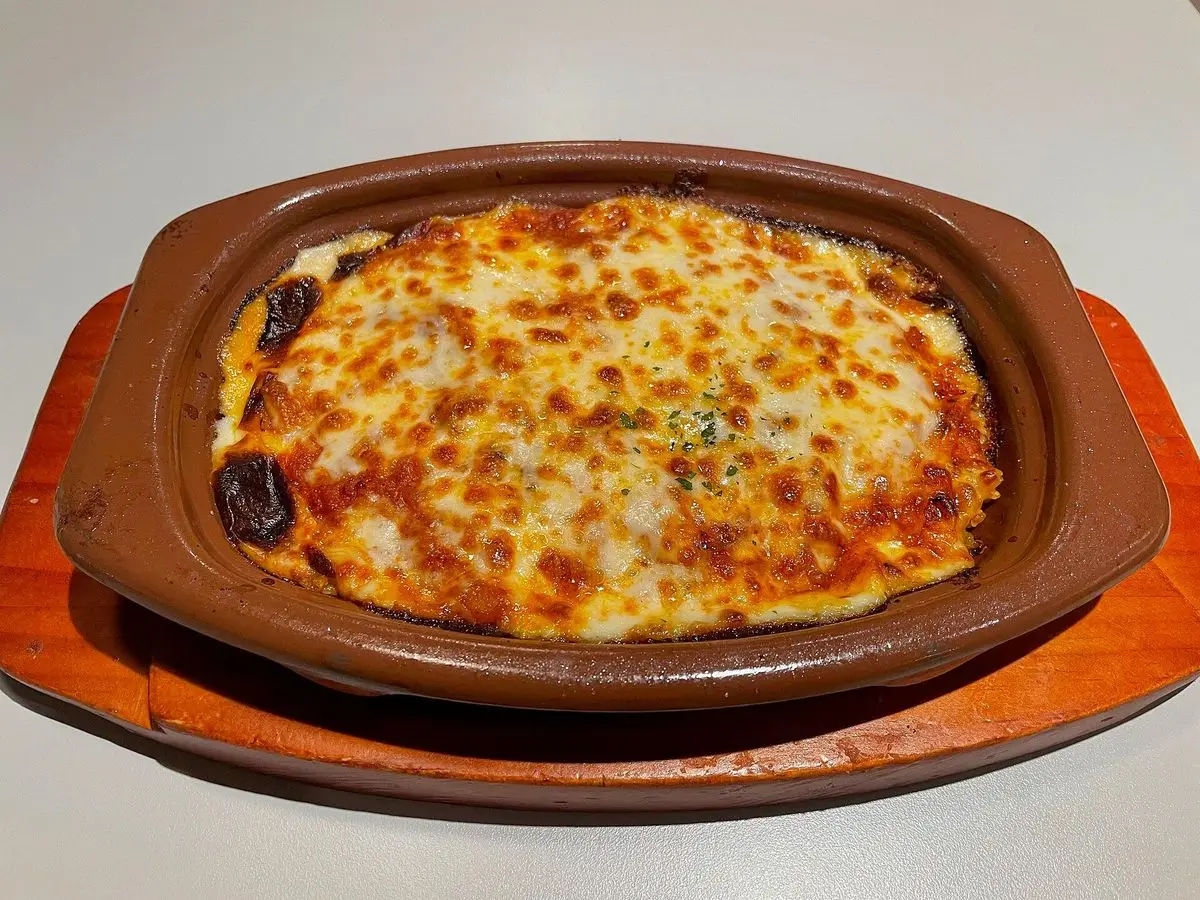 Fuente de arroz gratinado con queso dorado y salsa sobre una tabla de madera