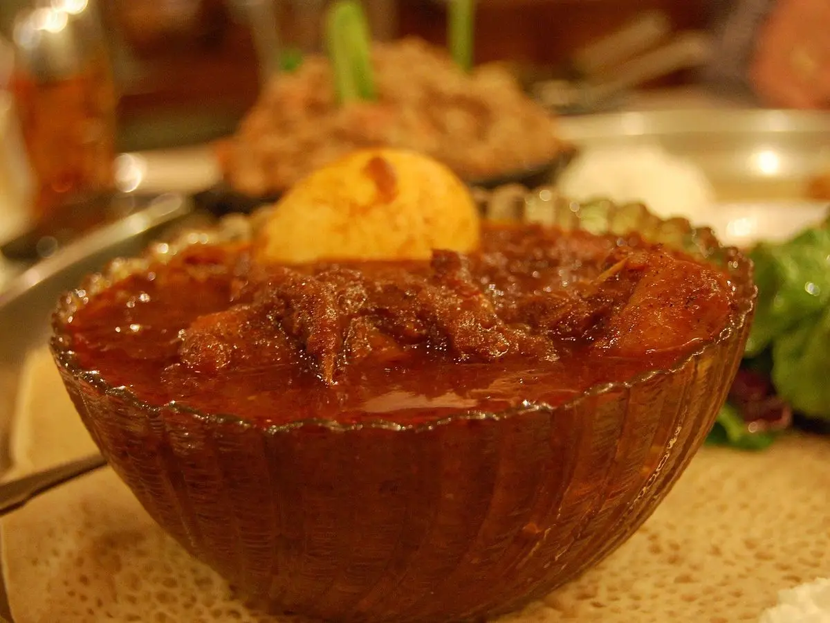 Cuenco de cristal con guiso etíope rojo especiado y huevo cocido sobre injera
