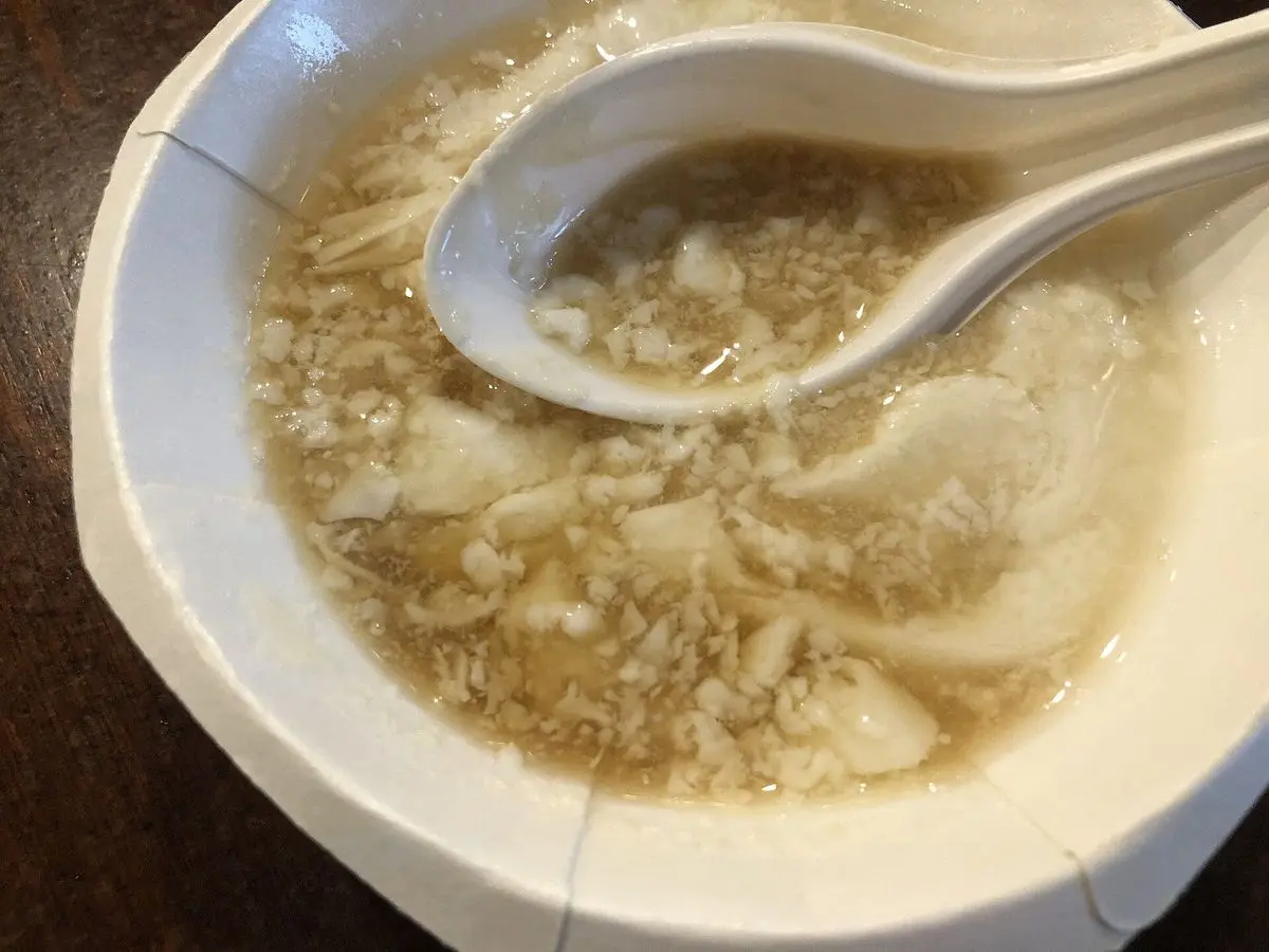 Cuenco de tofu sedoso con caldo y toppings y una cuchara de plástico